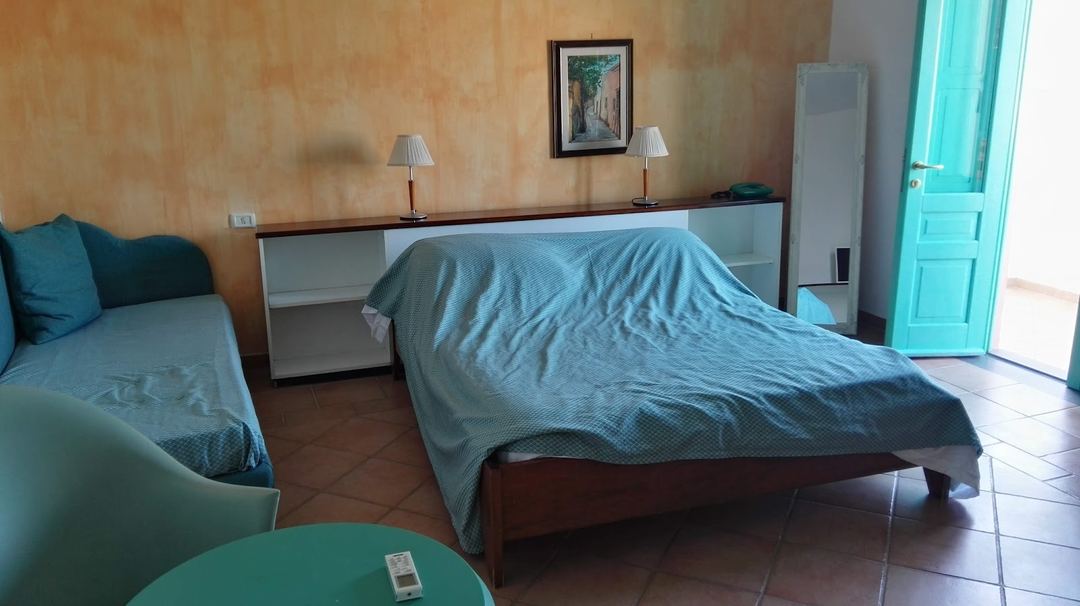 A hotel bedroom with two beds, terracotta-colored walls, and turquoise accents, featuring a desk with lamps and access to a balcony.